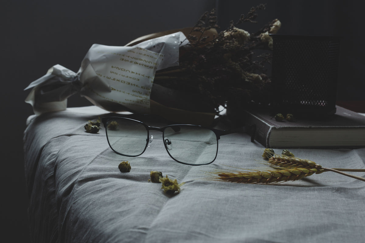 Black metal semi-rimless eyeglasses with light blue tinted lenses on linen table, artistic product photography