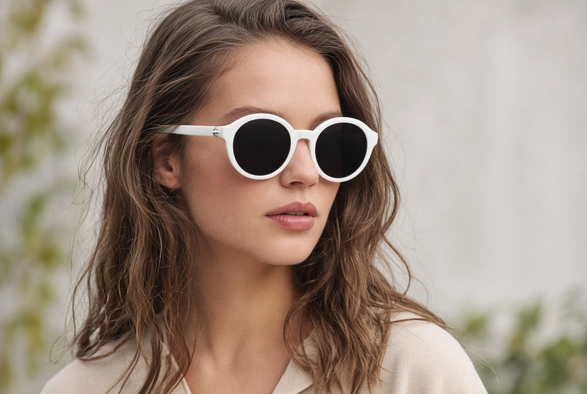 Woman with wavy brown hair wearing white round sunglasses with dark lenses, lifestyle product image