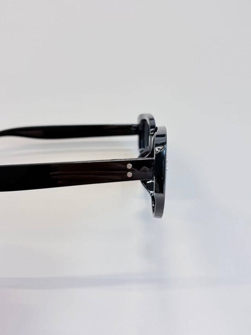 Close-up side view of black round-frame sunglasses with glossy acetate arms on a clean white background.
