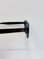 Close-up side view of black round-frame sunglasses with glossy acetate arms on a clean white background.