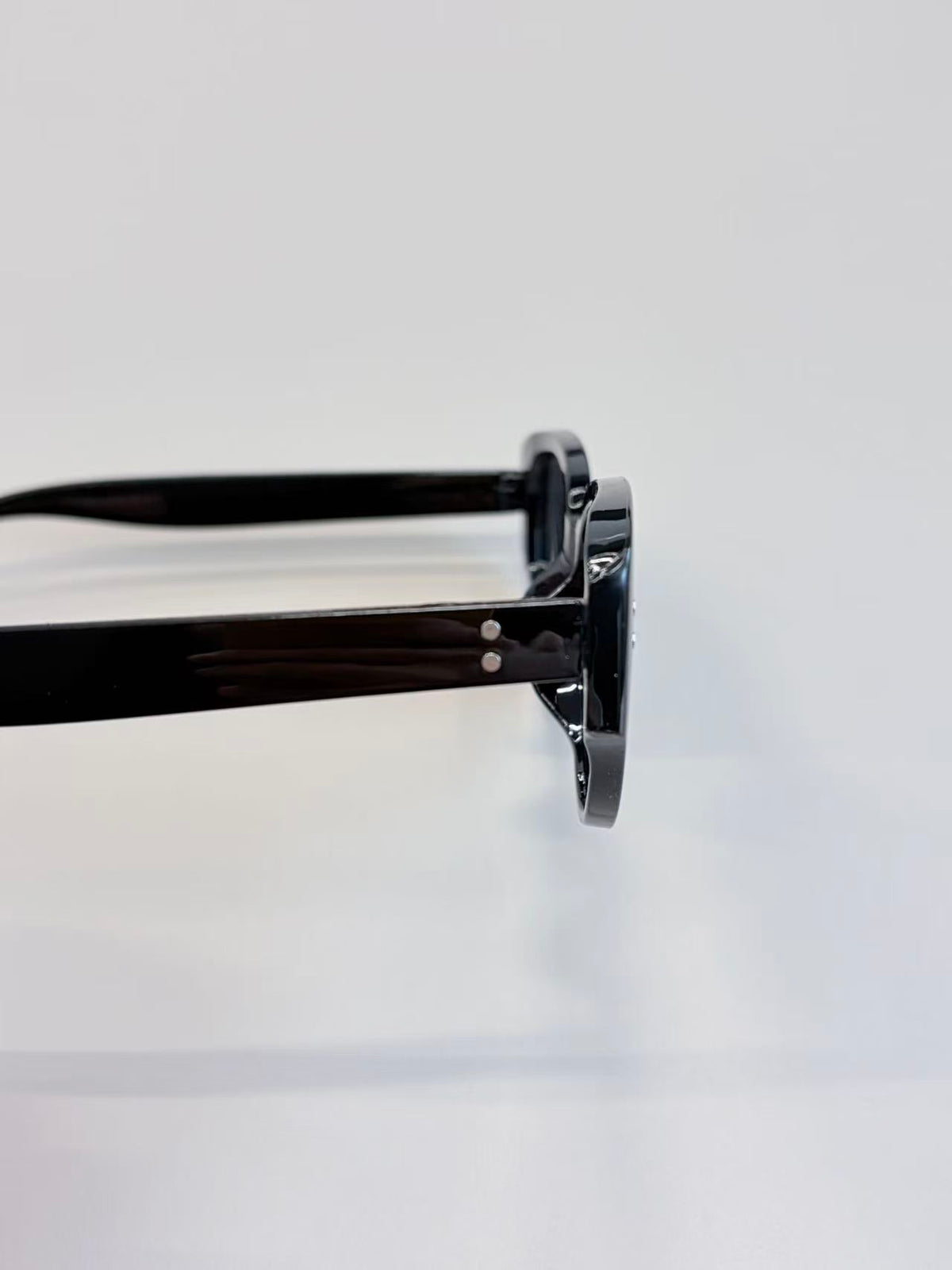 Close-up side view of black round-frame sunglasses with glossy acetate arms on a clean white background.